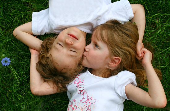A girl kissing a boy while laying in the grass