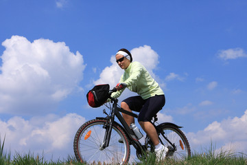 Fototapeta premium Young lady cycling, blue sky background