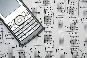 A closeup of a cellular phone over a sheetmusic