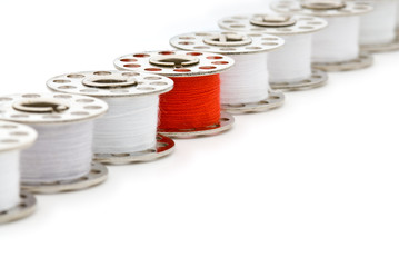 Bobbin of red thread among bobbins of white thread, isolated on