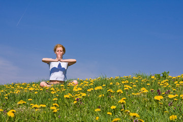 Naklejka na ściany i meble young female excercising yoga on flowery meadow