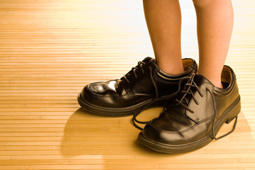 Big shoes to fill, child's feet in large black shoes, on wood fl - obrazy, fototapety, plakaty