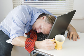 An exhausted businessman falls asleep on computer.