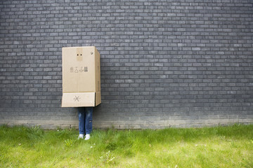 girl standing against a wall with a cardboard box over his head