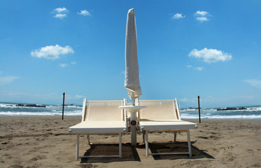 Fototapeta na wymiar coppia di lettini e ombrelloni bianchi in spiaggia