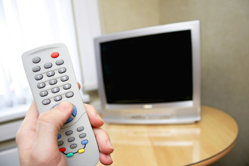 human hand holding remote control against tv