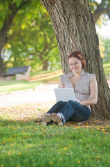 Female university student working on a laptop in green park