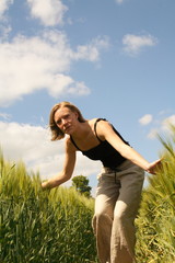 Frau geht auf den Betrachter zu, streicht über Getreideähren