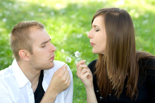 Couple blowing dandelion with flying seeds
