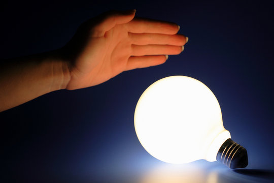 one glowing light bulb and female hand on a blue background.