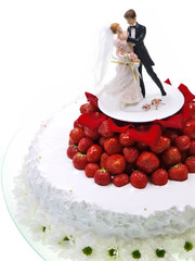 Hochzeitstorte mit weißen Chrysanthemen Blüten, weißer Zuckerguss und süße rote Erdbeeren wo Braut- und Bräutigamfiguren stehen