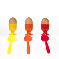 three eggs in colorful egg cups with colorful spoons
