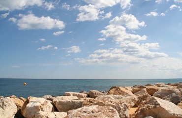 Fototapeta na wymiar Blue sky with clouds above blue sea and stones in front