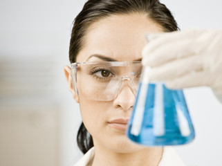 Female scientist looking at beaker of blue liquid - Powered by Adobe