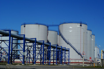 Obraz premium industrial pipelines and storage tanks against blue sky