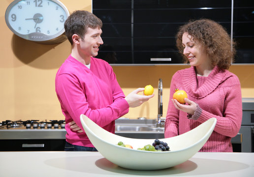 young couple on kitchen with fruits in hands
