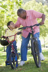 Obraz premium Grandfather and grandson on bikes outdoors smiling