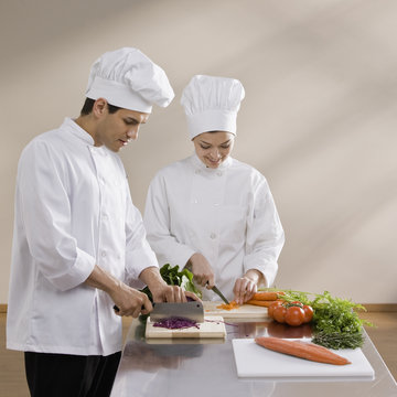 Male and female chef chopping vegetables