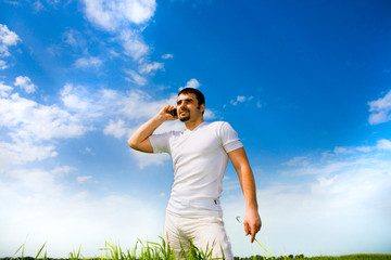 Man at the phone in the field under blue sky. In white dress