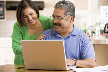 Couple in kitchen with laptop smiling