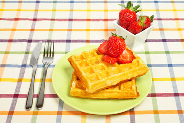 Waffles and strawberries on green plate.