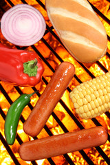 Hot dogs, bun, peppers, onion and corn on a barbecue grill