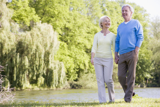 Couple Walking Outdoors At Park By Lake Smiling