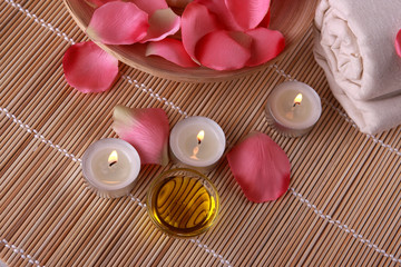 spa products with rose petals, oil container, towel and candles