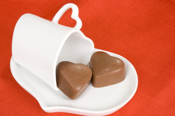 Heart shaped chocolates with cup and saucer on red background