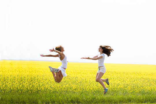 Two beautiful girl in white clothes jumps the yellow flowers