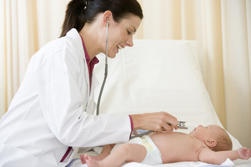 Obraz na płótnie Canvas Doctor giving checkup with stethoscope to baby in exam room smil