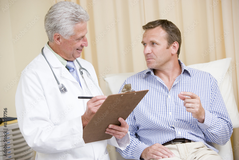 Wall mural Doctor writing on clipboard while giving man checkup in exam roo