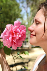 Fototapeta premium Young beautiful woman enjoys a smell of a pink rose