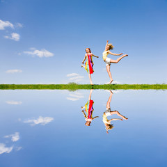 Two happy girl jumping together on green meadow. Reflected