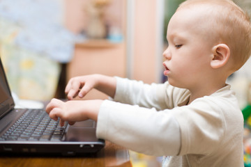 Little boy typing text on laptop at home
