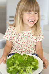 Young girl in kitchen eating broccoli smiling