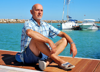 Uomo seduto con gambe incrociate su banchina di un porto