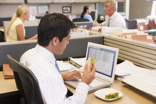 Businessman in cubicle eating sandwich