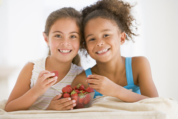 Two young girls eating strawberries in living room smiling