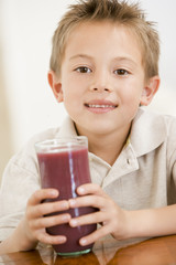 Young boy indoors drinking juice smiling