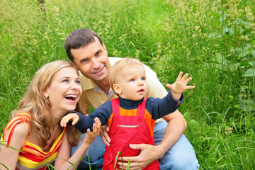 Parents with child sit in grass and look upwards