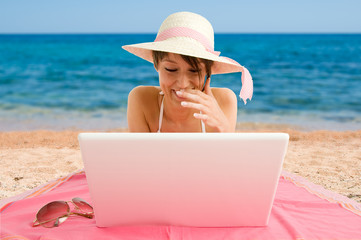 Smiling girl wearing bikini using laptop at the sea