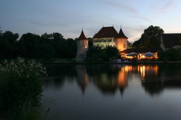 Fototapeta premium Castle with restaurant in front of a calm lake at dusk.