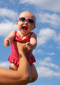 Happy Baby girl in swimsuit under clouds