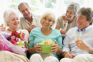 Five friends with champagne and gifts in living room smiling