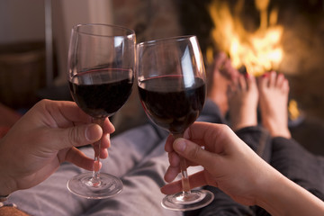 Feet warming at fireplace with hands holding wine