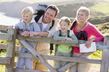 Family on cliffside path leaning on fence and smiling - obrazy, fototapety, plakaty