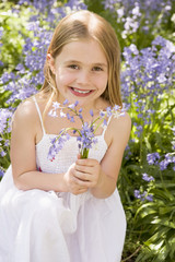 Young girl outdoors holding flowers smiling