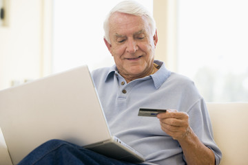 Fototapeta na wymiar Man in living room with laptop and credit card smiling