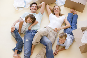 Family lying on floor by open boxes in new home smiling